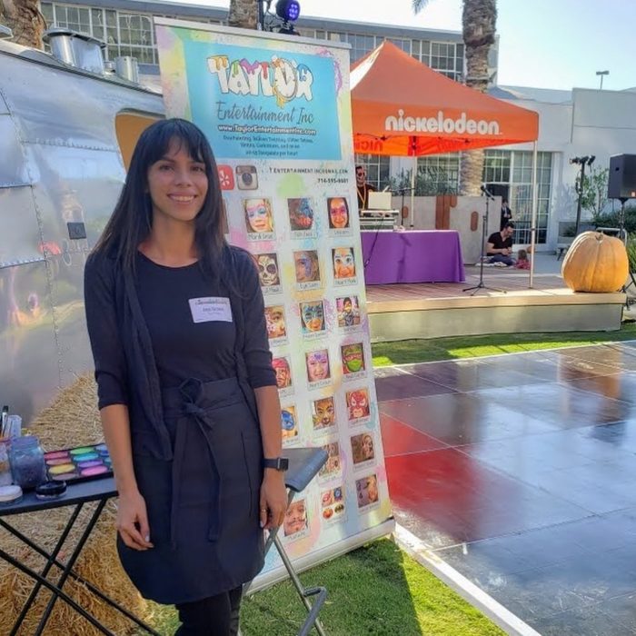 A Taylor Entertainment Inc. face painter at her setup, with the design board guests choose from and her paints laid out on the table